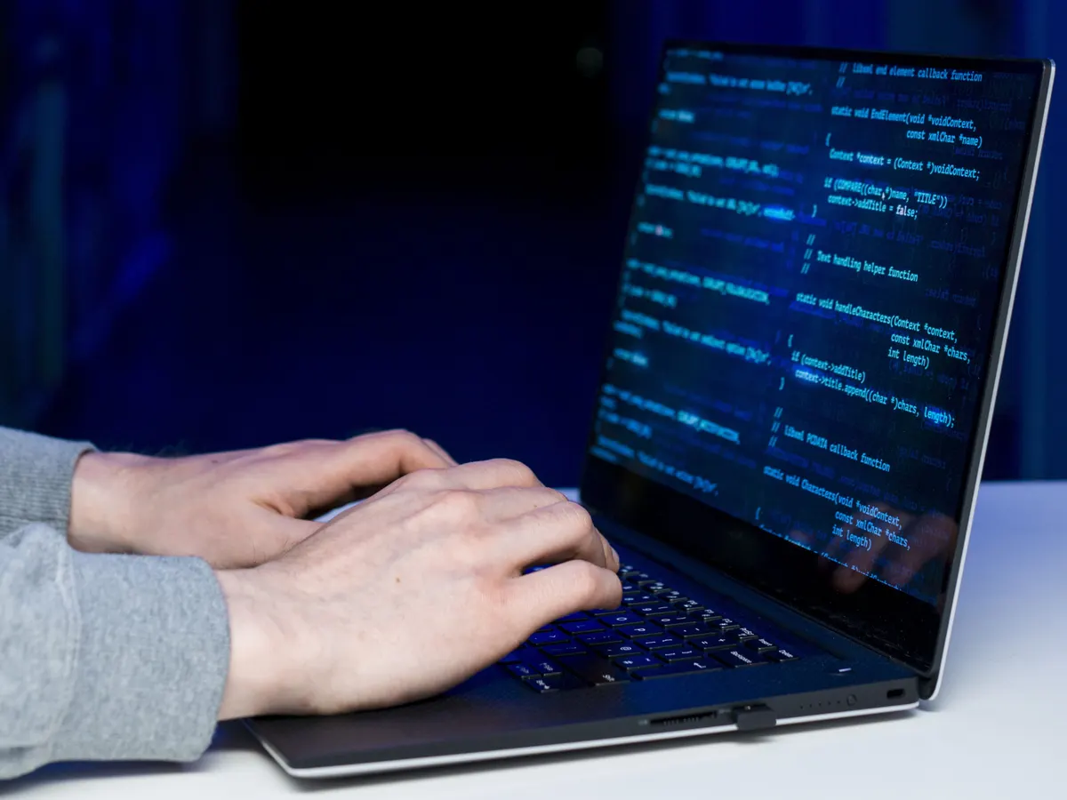A security analyst typing at a laptop showing code in a dimly lit server room